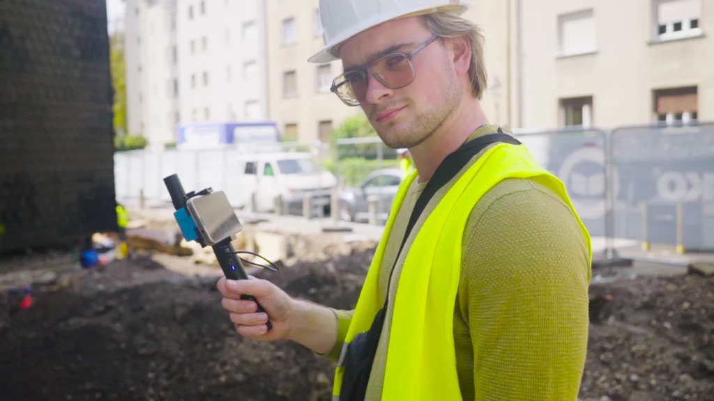 Land surveyor onsite holding a smartphone with attached RTK GNSS device