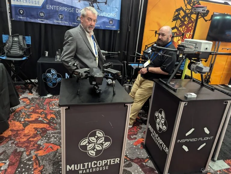 2 older men with beards standing behind their display drones at their booth at Commercial UAV expo