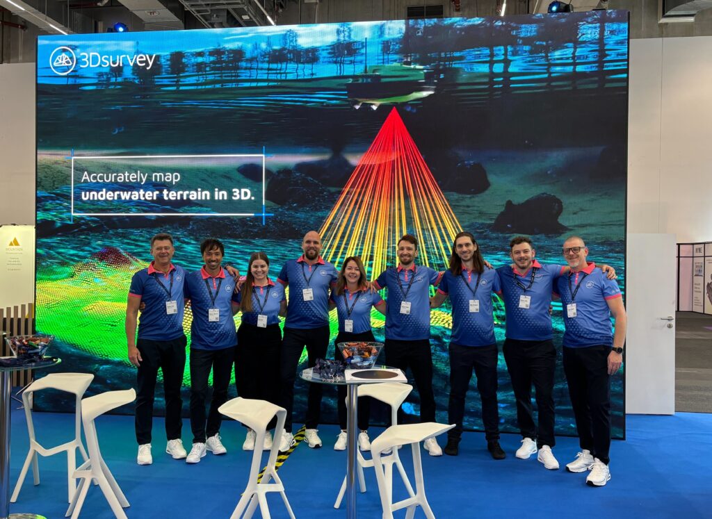 3Dsurvey team posing at their expo booth in front of a big LED screen