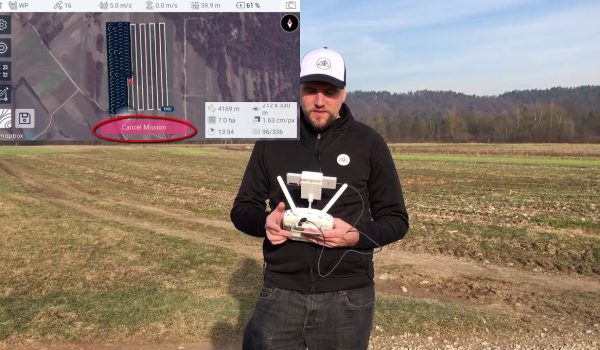 A drone pilot with a white cap holding drone controllers while standing in an open field